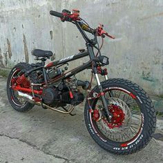 a red and black dirt bike parked next to a concrete wall with graffiti on it