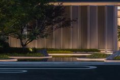 a building that is lit up at night with trees and bushes in front of it