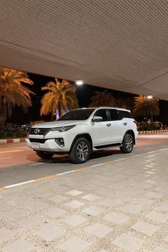 a white suv parked under an overpass in a parking lot at night with palm trees behind it