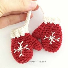 a hand is holding two crocheted red mittens with white snowflakes on them