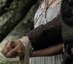 a woman in an old fashioned dress holding onto a pair of gloves while standing next to a tree