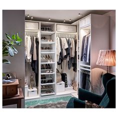 an open closet with clothes and shoes on shelves next to a lamp in a living room