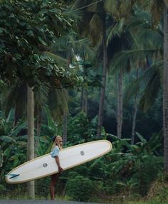 a woman holding a surfboard on the side of a road in front of palm trees