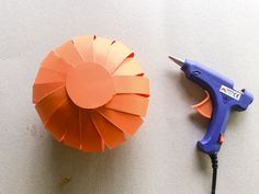 an orange paper flower next to a blue plastic blow dryer on a white surface