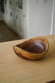 a wooden bowl sitting on top of a table next to a white cupboards in a kitchen