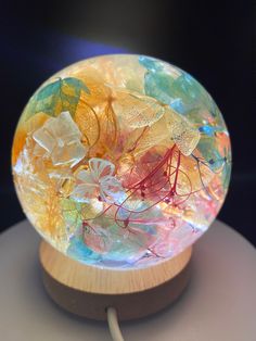 a glass ball with colorful leaves in it sitting on a wooden stand and plugged into a charger