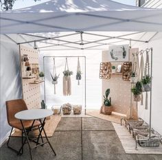 a white tent with plants hanging on the wall and a table in front of it