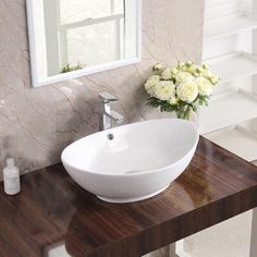 a white bowl sink sitting on top of a wooden counter next to a vase with flowers