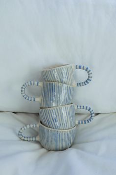 four blue and white striped mugs stacked on top of each other in the middle of a bed