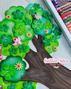 a tree with lots of green leaves and flowers painted on it, next to crayons