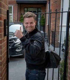 a man standing in front of a gate giving the thumbs up sign with his hand