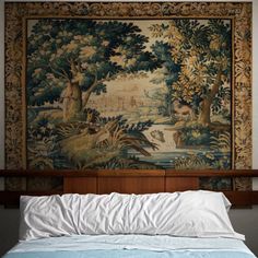 a large tapestry hangs above a bed with white sheets and pillows on top of it