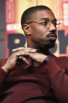 a man with glasses sitting in front of a microphone and looking off to the side