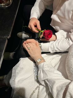 a man and woman sitting next to each other holding hands with a rose in their lap