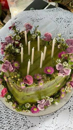 a green cake with flowers and candles on it sitting on top of a doily