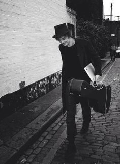 a man walking down the street carrying a suitcase and a hat on top of his head