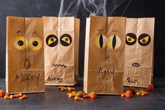 three paper bags with faces and eyes on them, one has candy candies in front of it