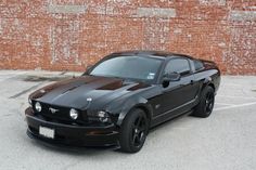 a black mustang car parked in a parking lot next to a brick wall and building