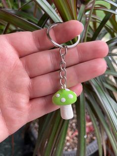 a hand holding a key chain with a green mushroom charm on it's end