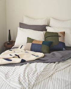 an unmade bed with several pillows and blankets on top of it, next to a night stand