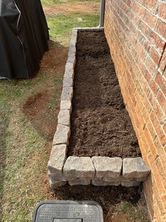 a garden bed with dirt in it next to a brick wall