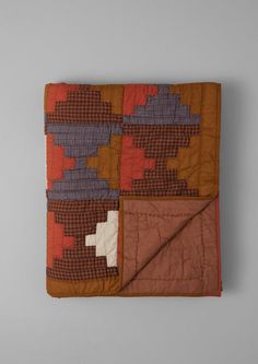 an orange and brown quilted blanket sitting on top of a gray table next to a white wall