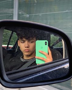 a young man taking a selfie in the side mirror of a car with his cell phone