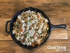 a skillet filled with rice and vegetables on top of a wooden table