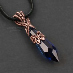 a necklace with a blue crystal stone and an intricate design on the end, sitting on a black cord