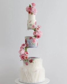 a three tiered cake with pink flowers on top and white frosting in the middle