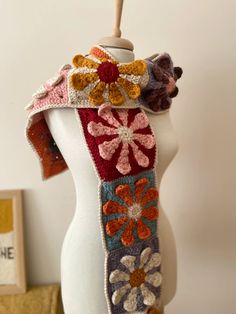 a white mannequin wearing a multicolored knitted scarf with flowers on it