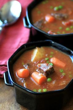 two black bowls filled with stew and carrots on top of a wooden table next to a red napkin