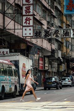 a woman walking across a street in front of tall buildings with chinese writing on them