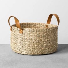 a woven basket with leather handles on the top is shown in front of a white wall