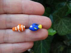 two small toy fish sitting on top of a persons finger in front of some plants