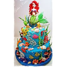 the little mermaid is sitting on top of this blue cake with corals and seaweed