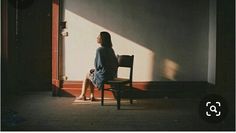 a woman sitting in a chair looking out the window with her shadow on the wall