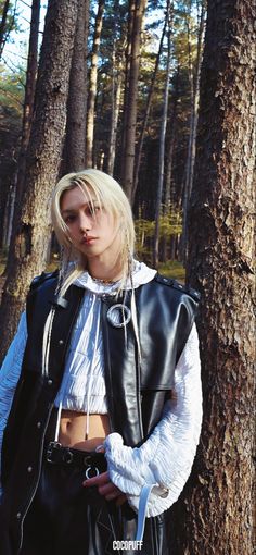 a woman standing next to a tree wearing a leather jacket and white cropped top