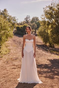 a woman in a white dress standing on a dirt road