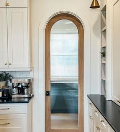 a kitchen with white cabinets and black counter tops next to an arched glass door that leads into the kitchen