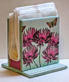 a stack of folded books sitting on top of a table next to a vase filled with flowers