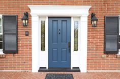 a blue front door with two black shutters on the side of a brick building