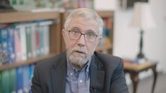 an older man with glasses is sitting in front of bookshelves