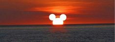 the sun is setting over an ocean with a mickey mouse head in the middle of it