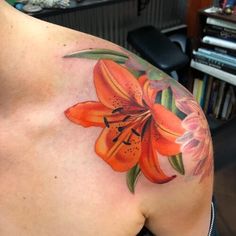 an orange lily tattoo on the back of a woman's left shoulder and arm