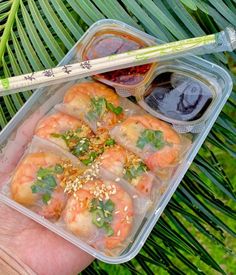 a hand holding a plastic container filled with food and chopsticks next to it