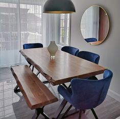 a dining room table with blue chairs and a round mirror on the wall above it