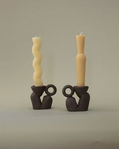 two candles sitting next to each other in front of a gray background and one candle has an odd shape