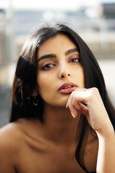 a woman with long dark hair is looking off to the side and has her hand on her chin