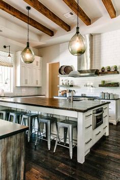 a large kitchen with wooden floors and white cabinets, two pendant lights hanging over the island